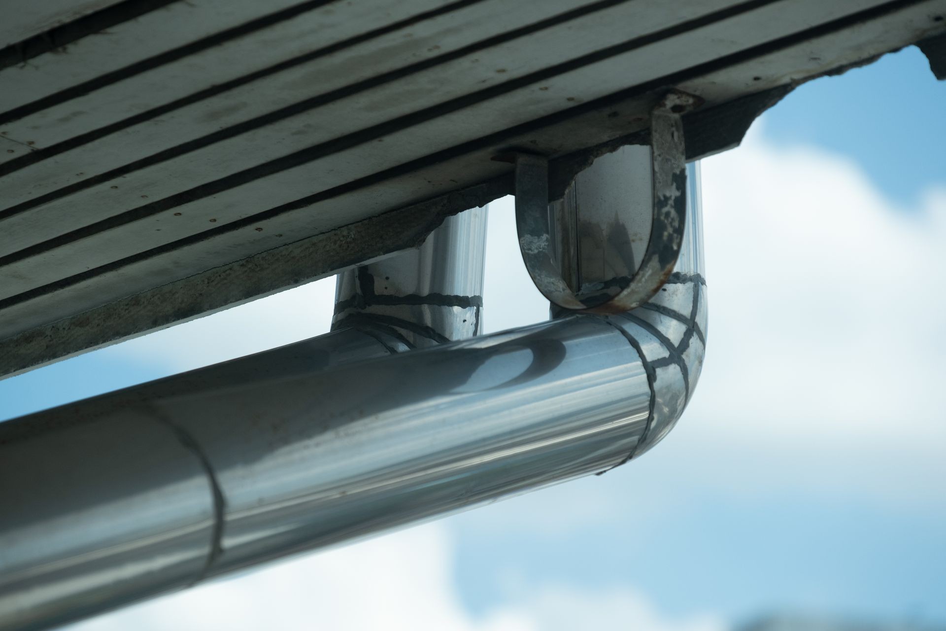Rain gutters on a home. There is a blue sky with a fluffy white cloud in the background. House trough on roof and blue sky and cloudy - can use to display or montage on product. Rain gutters on a home. There is a blue sky with a fluffy white cloud in the background. House trough on roof and blue sky and cloudy - can use to display or montage on product.